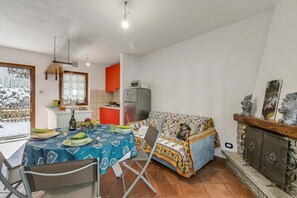 A dining area with a table set for two, a sofa, and a kitchen in the background. - La Casa Di Dada With Terrace and Garden (Oulx)