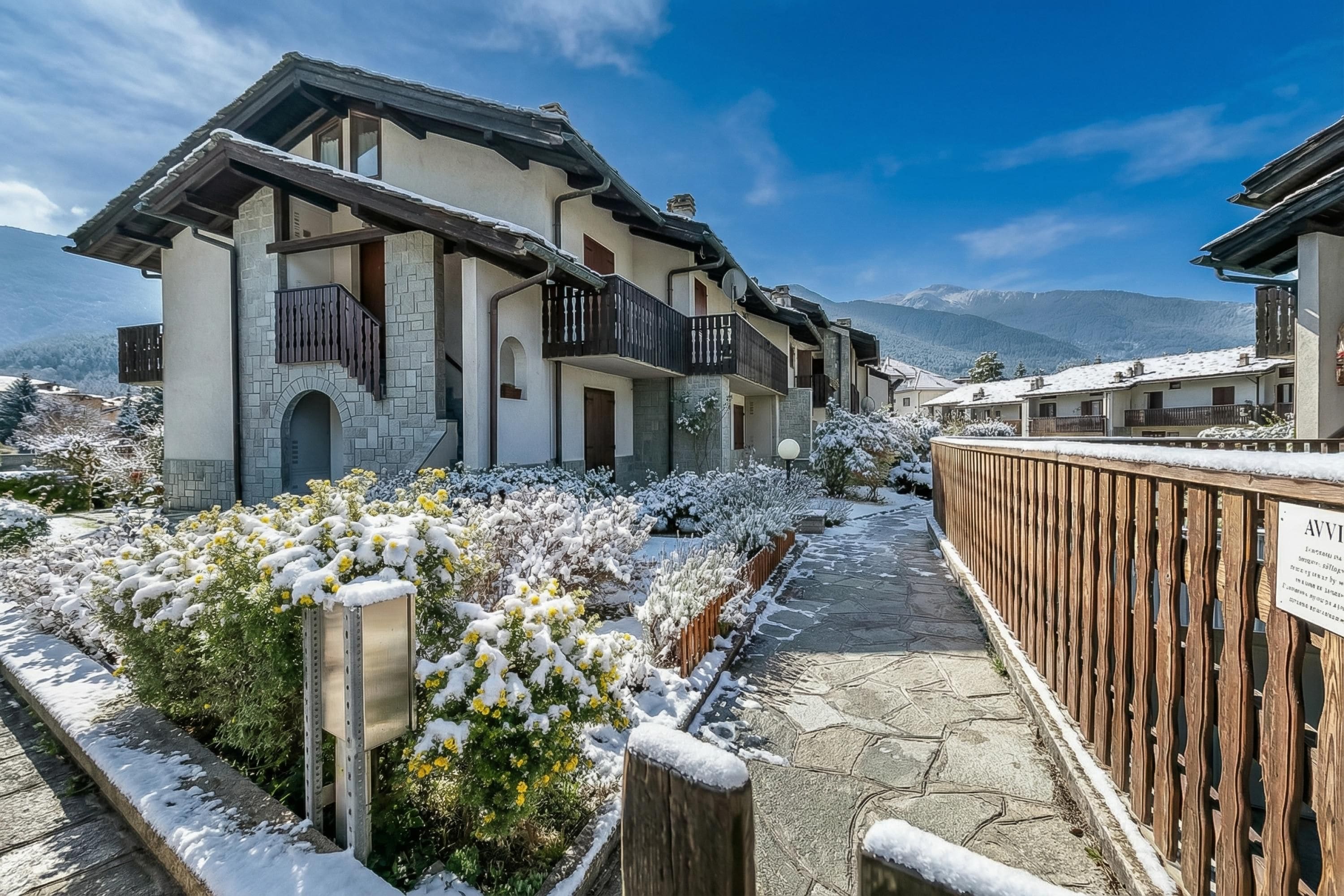 A snow-covered residential area with houses featuring balconies and stone walls.