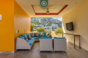 A modern hotel lobby with a curved sofa, a ceiling fan, and a view of surrounding buildings.
