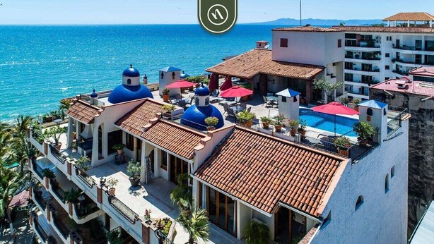 A coastal hotel with multiple balconies, a swimming pool, and a view of the sea.