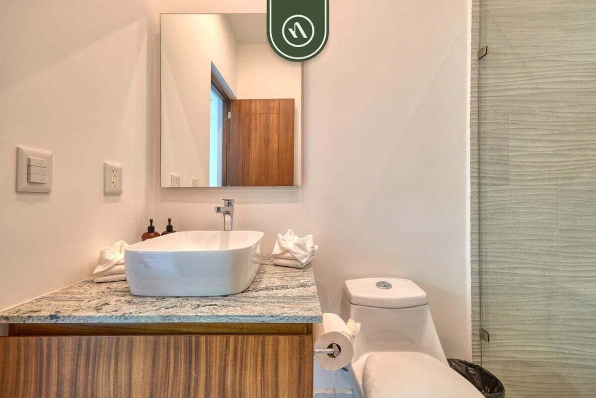 A bathroom with a white sink, a mirror, a wooden vanity, a toilet, and a towel rack.