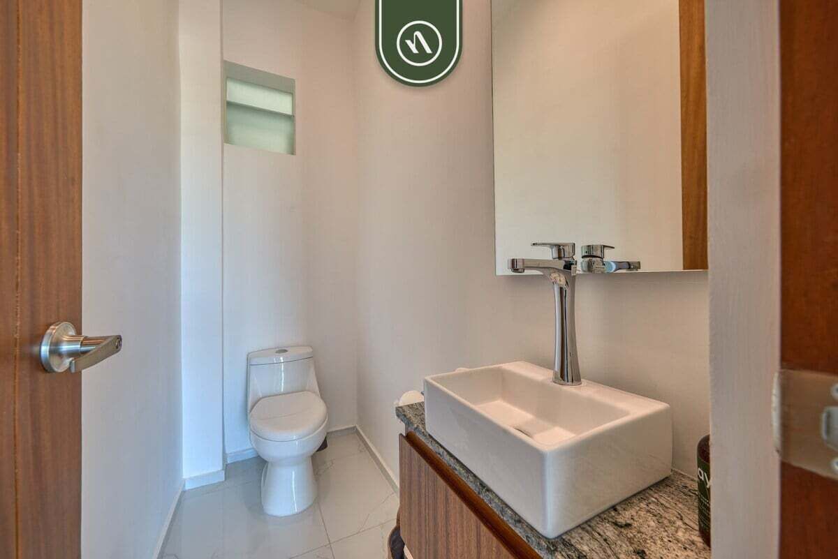 A bathroom with a white toilet, a rectangular sink with a mirror above it, and a wooden door.