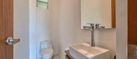 A bathroom with a white toilet, a rectangular sink with a mirror above it, and a wooden door.