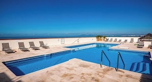 Ein Pool auf dem Dach mit klarem, blauem Wasser, umgeben von Liegestühlen und Blick aufs Meer.