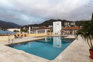 A swimming pool with a tiled deck, lounge chairs, and a view of buildings and mountains in the background.