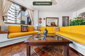 A living room with yellow sofas, a coffee table, and a view of a building outside. - 305-VistadelSol | 2BR/2BA Puerto Vallarta, Ocean View (Puerto Vallarta)