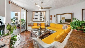 Un soggiorno con un divano giallo, un tavolino in vetro, una ventola a soffitto e un grande specchio.