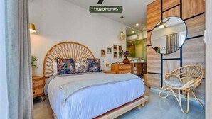 A modern bedroom with a large bed, a round mirror, wicker chairs, and a wooden wall panel. - Cozy 1Br Apt - Pool - GYM - 2 Min to the Beach (Bucerías)