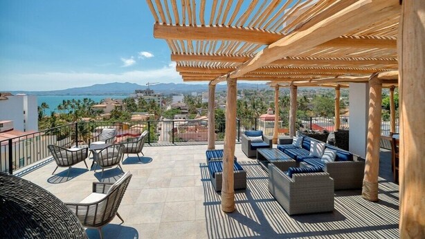 A rooftop terrace with outdoor seating, a wooden pergola, and a view of the city and mountains. - Cozy 1Br Apt - Pool - GYM - 2 Min to the Beach (Bucerías)