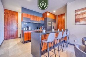A modern kitchen with wooden cabinets, a central island with bar stools, a built-in oven, and a refrigerator.