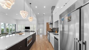 A modern kitchen with a large island, stainless steel appliances, and pendant lighting. - Walk to Beach + Pool, Hot Tub & Game Room | 30A Ohana Grande by AvantStay (Santa Rosa Beach)