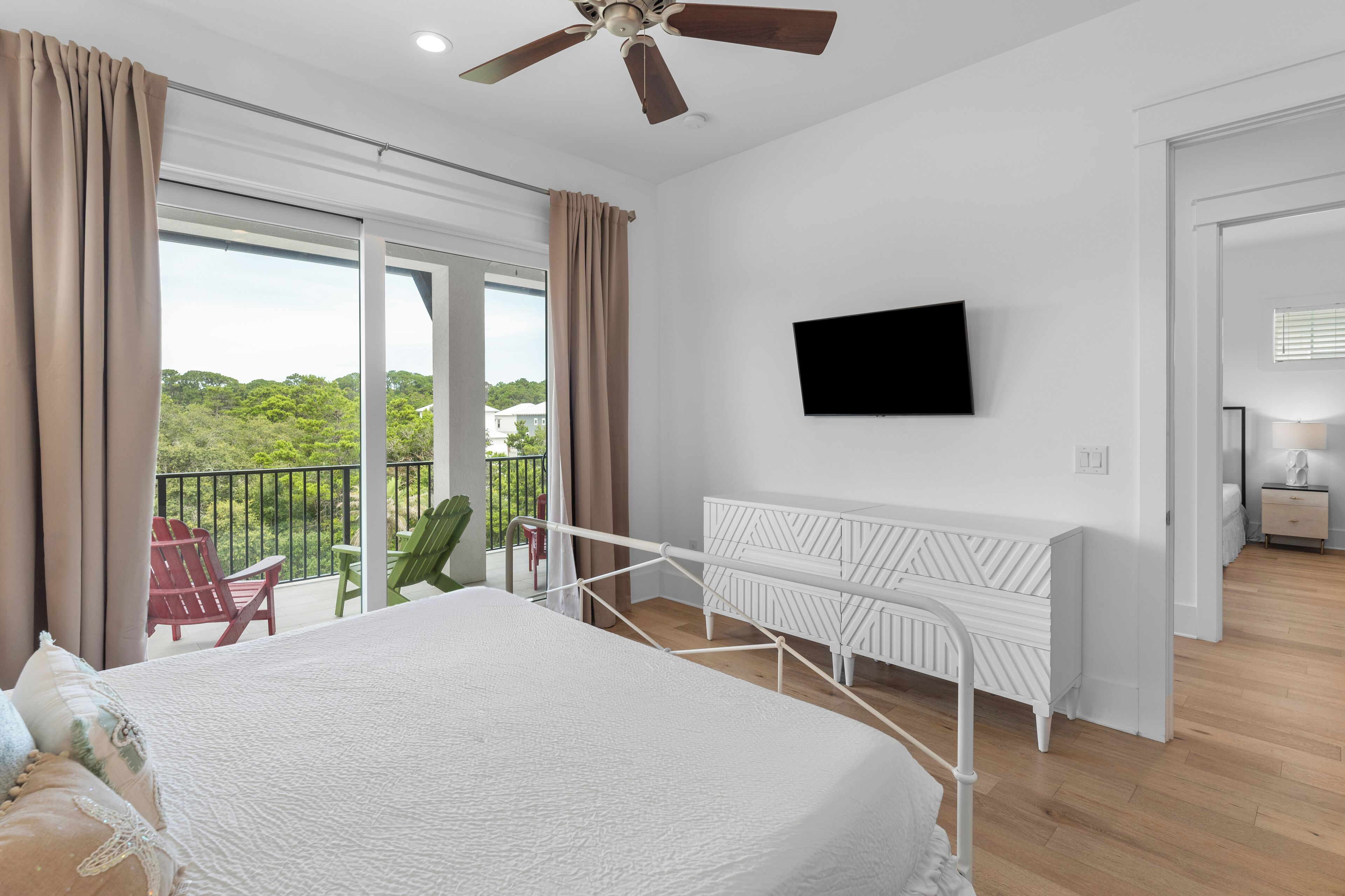 Een slaapkamer met een bed, een aan de muur bevestigde televisie, een balkon met stoelen en een plafondventilator.