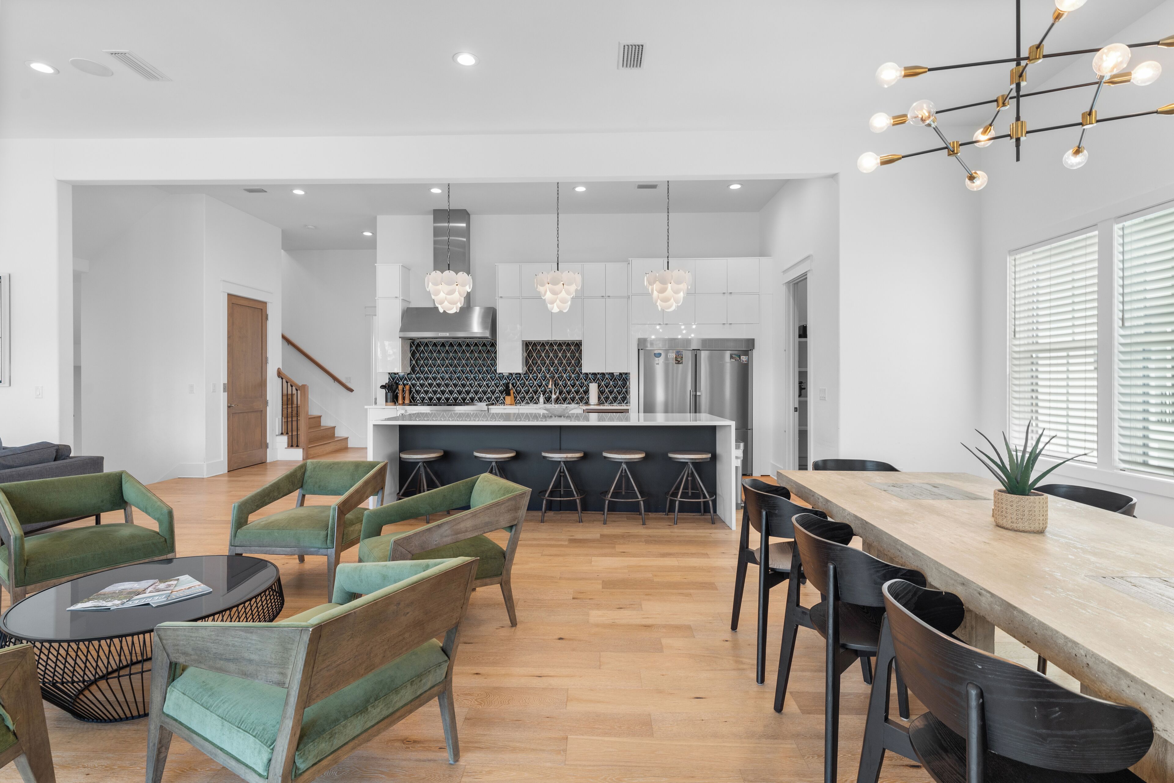 A modern kitchen with white cabinets, a central island, and bar stools. There is a dining area with a wooden table and chairs.
