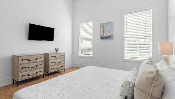 A bedroom with a large bed, two bedside tables, a flat-screen TV mounted on the wall, and two windows with blinds. - Walk to Beach + Pool, Hot Tub & Game Room | 30A Ohana Grande by AvantStay (Santa Rosa Beach)