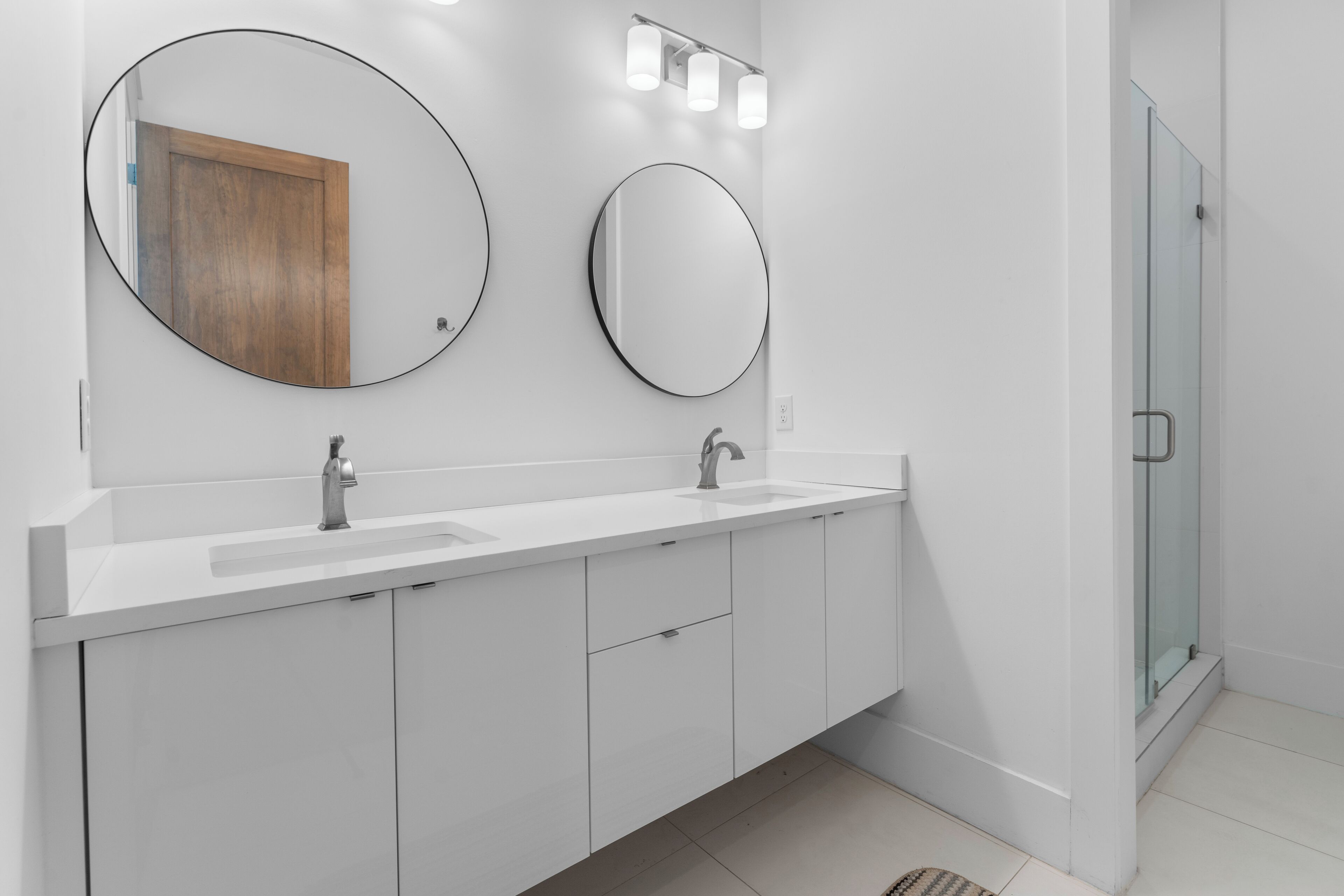 A modern bathroom with two sinks, a large mirror, and a glass shower enclosure.