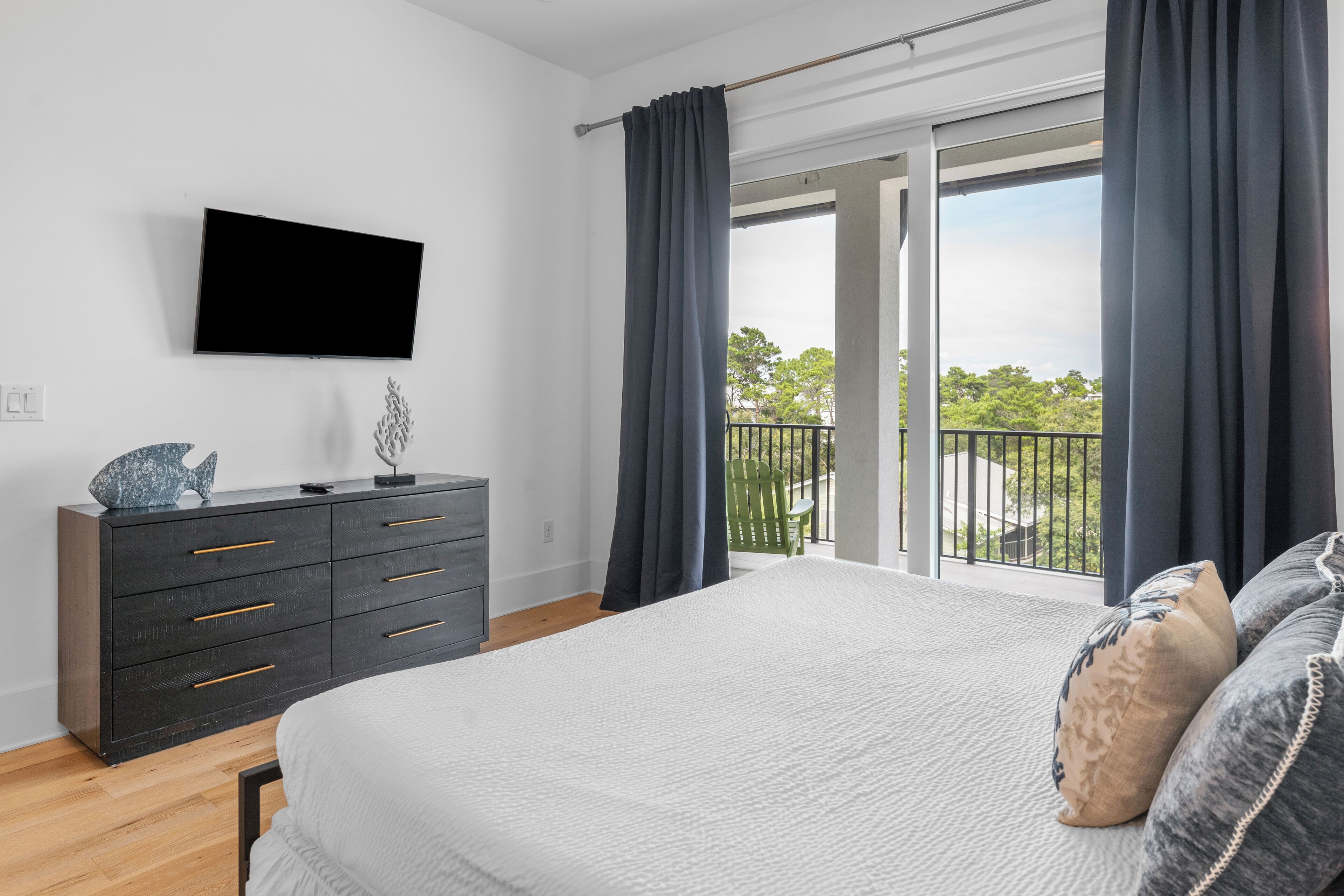 A bedroom with a large bed, a dresser, a flat-screen TV, and a balcony with a view.