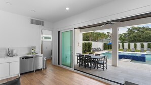 A modern kitchen with a dishwasher, a dining area with a table and chairs, and a sliding glass door leading to a pool area. - Walk to Beach + Pool, Hot Tub & Game Room | 30A Ohana Grande by AvantStay (Santa Rosa Beach)