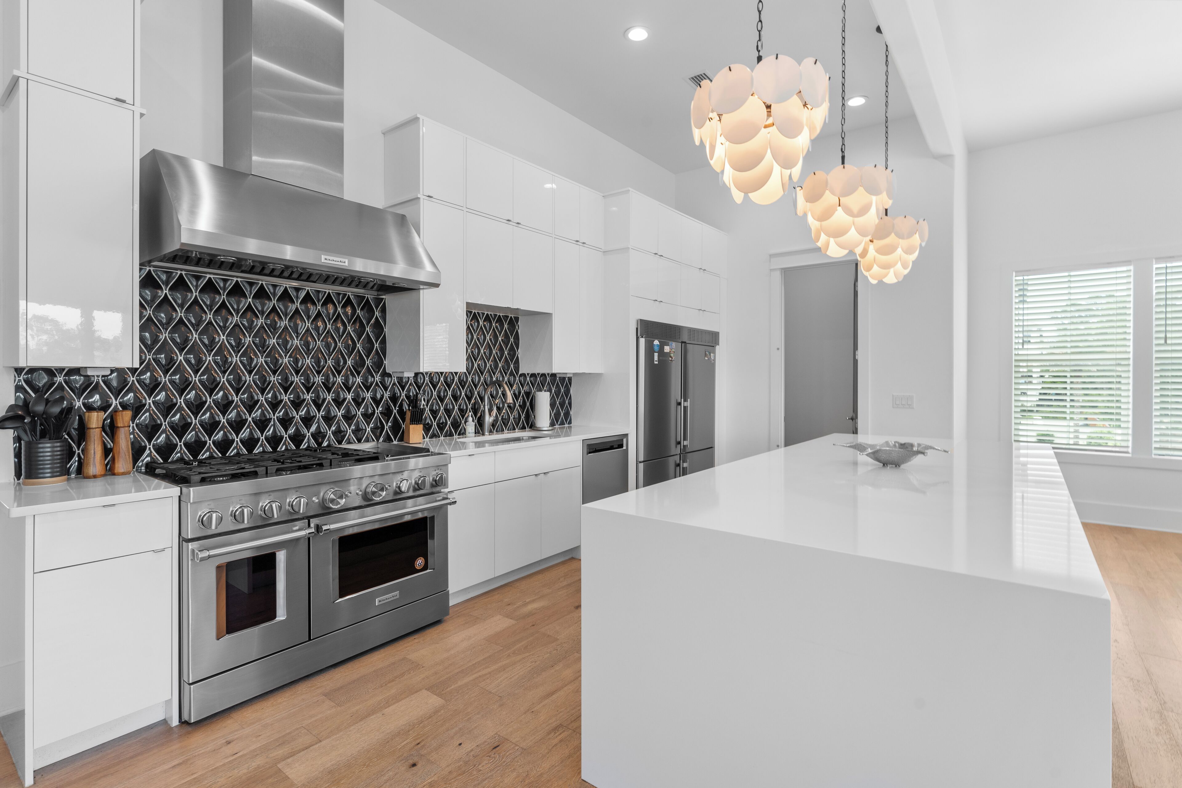 Een moderne keuken met witte kasten, een roestvrijstalen afzuigkap, een inbouwoven en een groot eiland met een witte aanrechtblad.