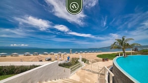 A resort with a swimming pool, beach, and a staircase leading to a terrace.