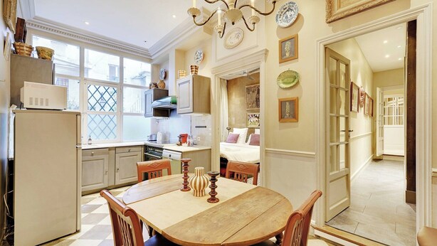 Una cocina con una mesa de comedor, sillas y un refrigerador. Hay armarios, un microondas y una ventana con vistas.