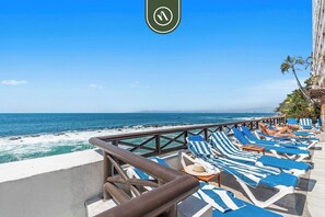 Un balcon donnant sur la mer, avec des fauteuils de jardin à rayures bleues et blanches, une balustrade et une vue sur l’océan.