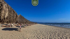 Ein Strand mit reetgedeckten Sonnenschirmen und Holzbänken.