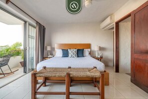 Une chambre à coucher comprenant un lit, des tables de chevet, une tête de lit en bois, un balcon avec une chaise et une porte-fenêtre coulissante.