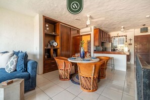 A living room with a sofa, a dining table with chairs, a kitchen area, and a ceiling fan.