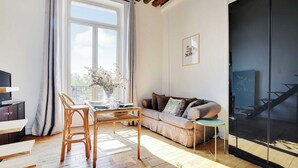 Un salon moderne avec un plancher en bois, un canapé, une table à manger avec des chaises et une grande fenêtre avec des rideaux.
