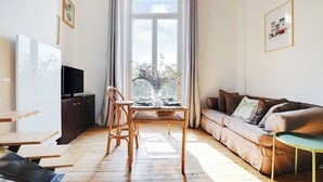 Un salon avec un canapé, une table à manger et des chaises, un téléviseur posé sur un meuble et une fenêtre avec des rideaux.