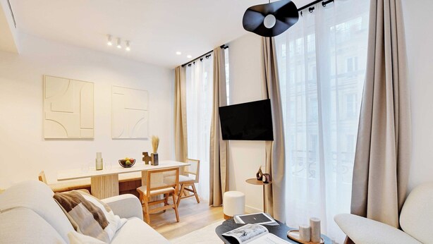 Una sala de estar moderna con un sofá, una mesa de centro con revistas, un televisor y un comedor con una mesa y sillas.