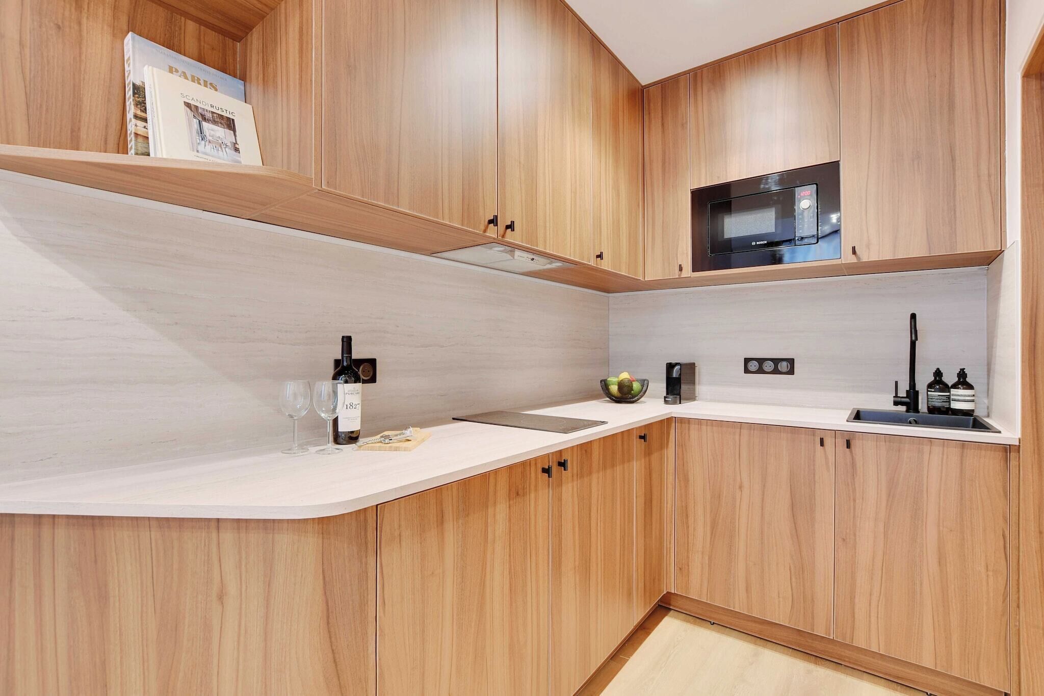 Una cucina moderna con mobili in legno, un forno a microonde e una bottiglia di vino sul piano di lavoro.