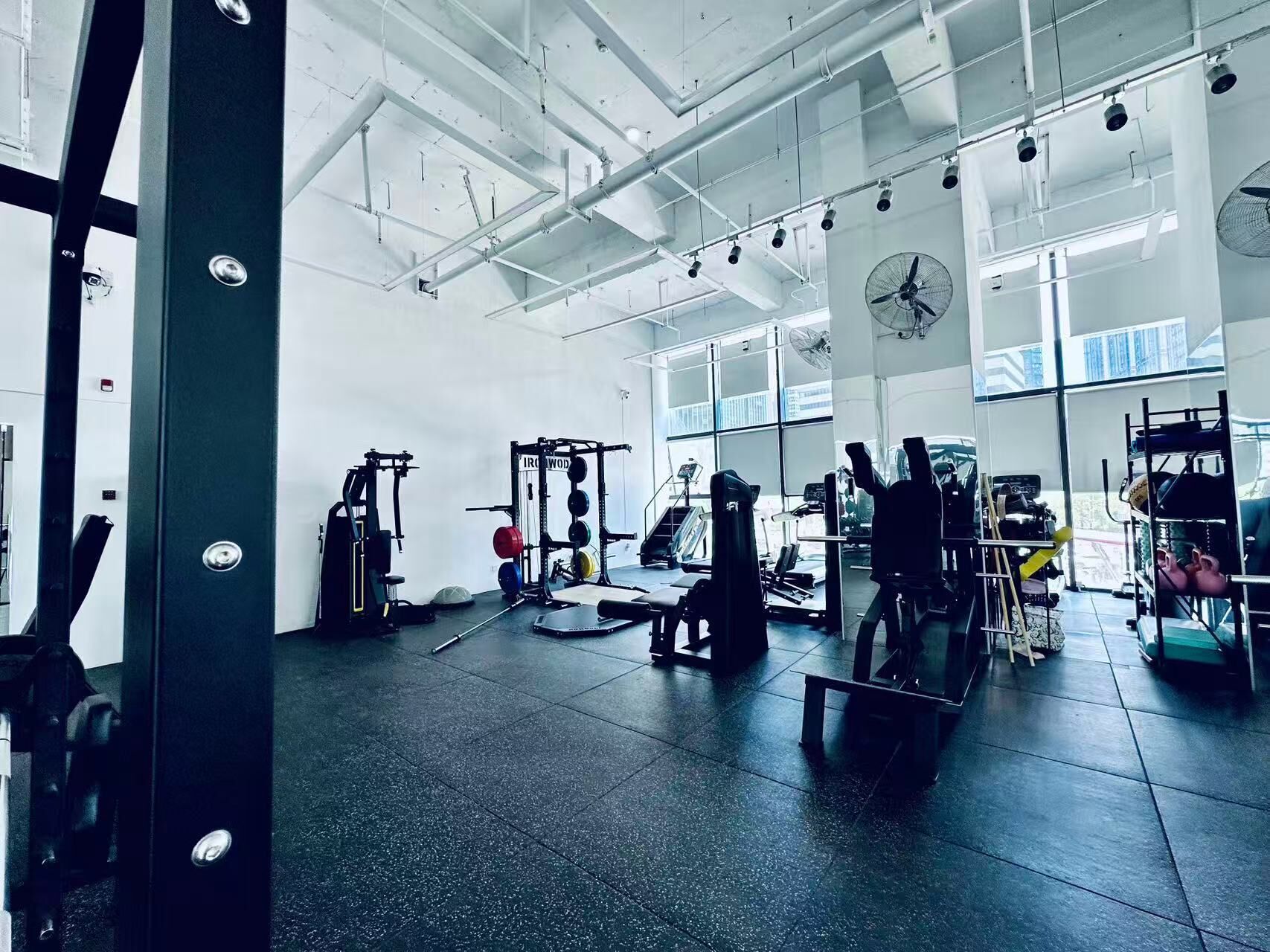A gym with various exercise equipment, large windows, and a high ceiling.
