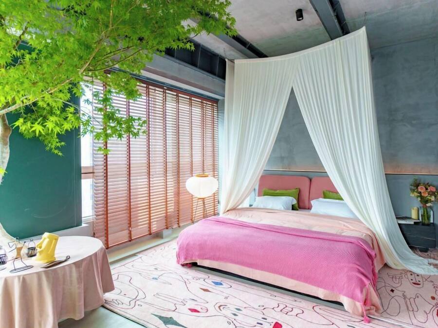 Um quarto com cama, mesa de cabeceira, abajur e janela com persianas.
