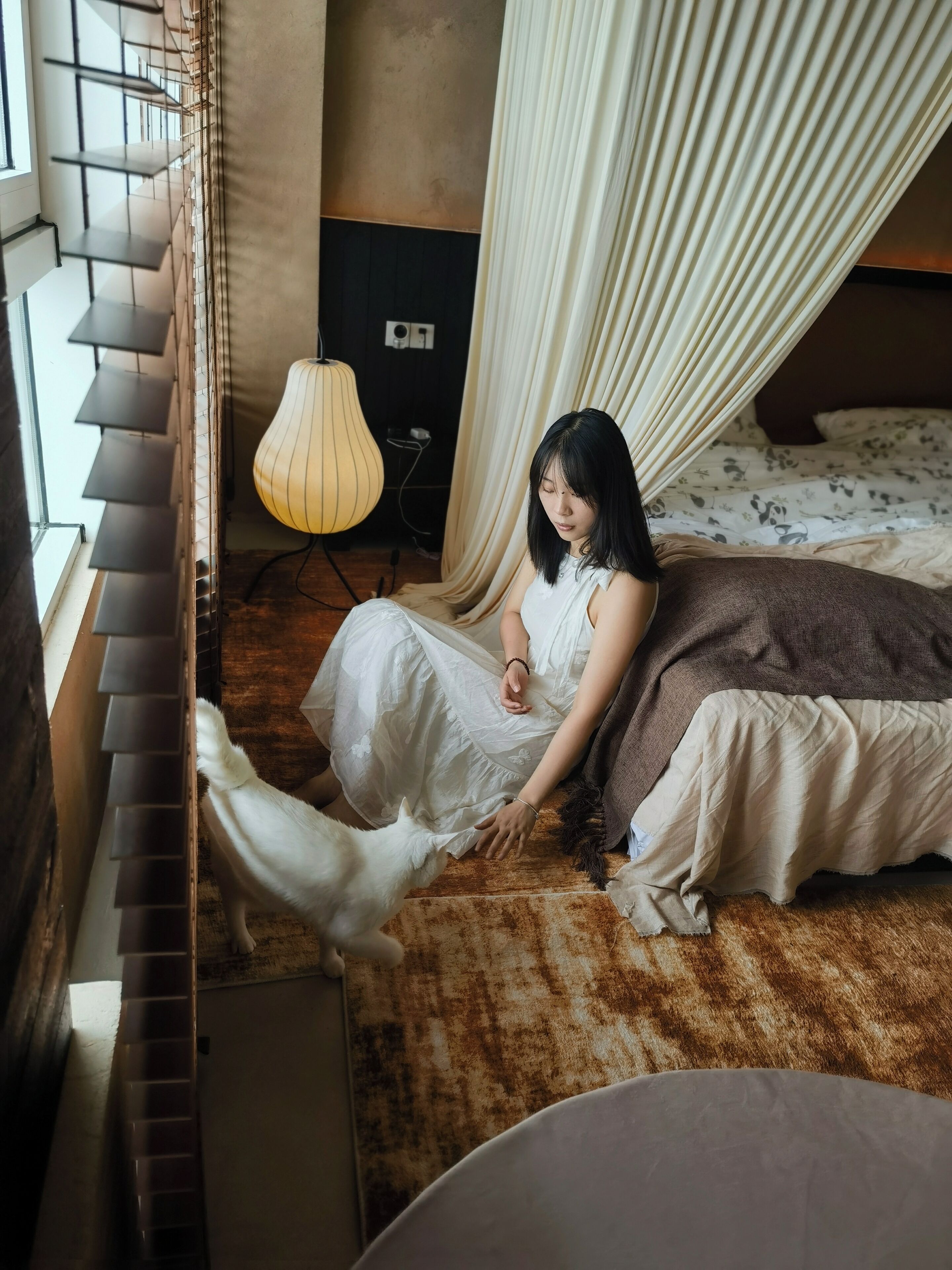 A room with a bed, a window with blinds, a lamp, and a curtain.