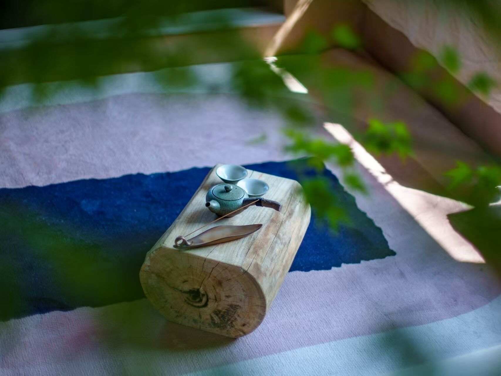 Un bloque de madera con una tetera y tazas sobre una tela azul y blanca a rayas.
