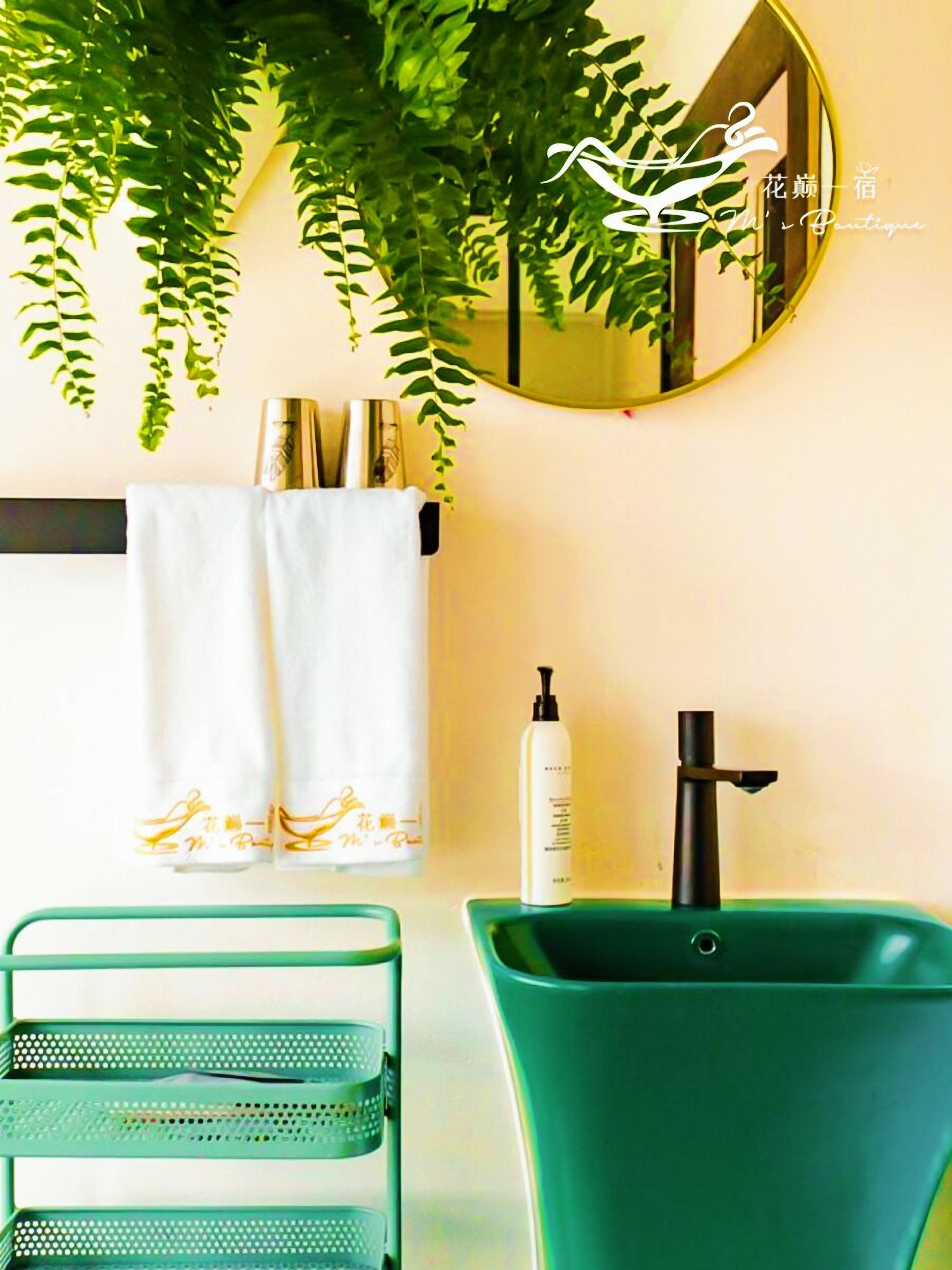 A bathroom with a green sink, a mirror, and a plant.