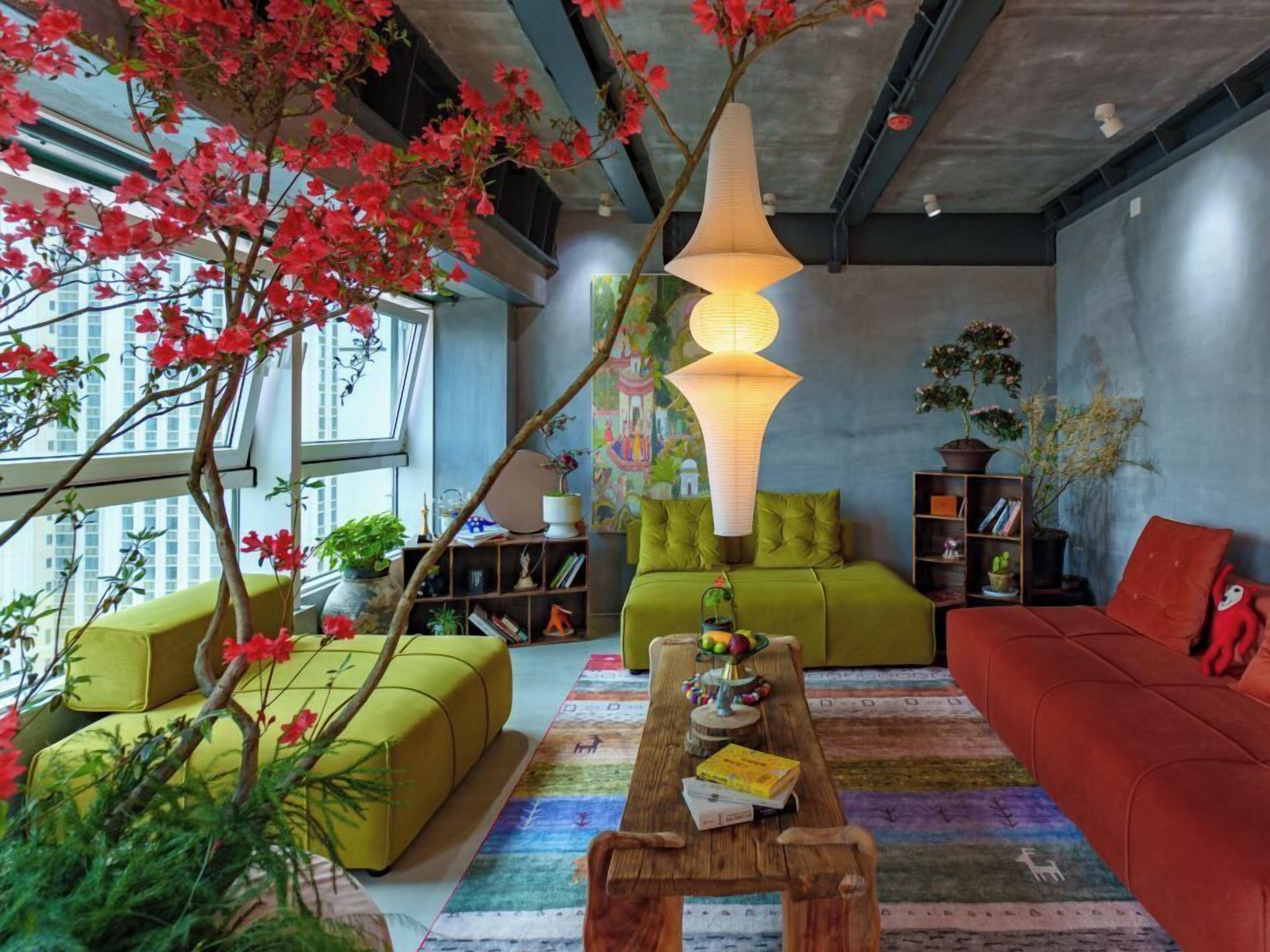 A modern living room with green sofas, a wooden coffee table, and a large window with red flowers.
