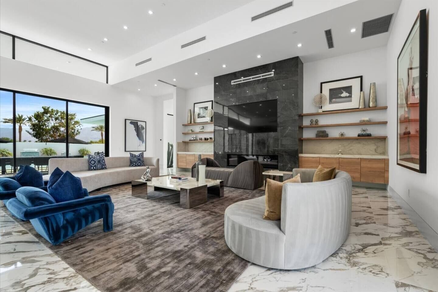 A spacious living room with a large window, a fireplace, and a kitchen area with marble countertops.