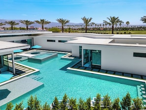 Un espace piscine moderne doté de plusieurs piscines, d’une eau d’un bleu cristallin et entouré de palmiers.