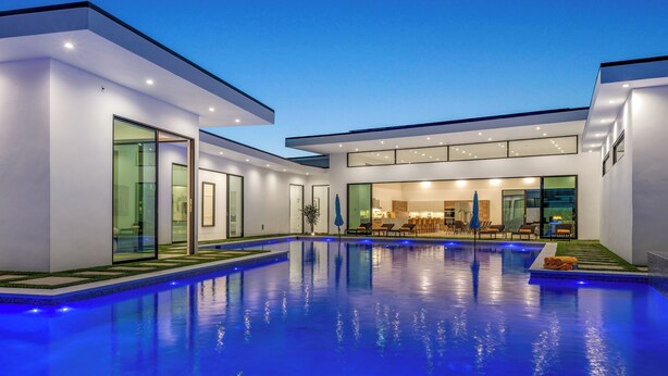A modern house with a swimming pool, large windows, and a well-lit interior. - Sleeps 17 | Private Pool + Pickleball Court + Fire Pit • Near La Quinta | Bravo (Indio)