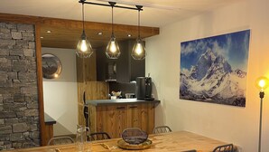 A modern dining area with a wooden table, metal chairs, and a bench. There is a kitchen in the background with a refrigerator and a coffee machine. - New Le Corbier for 10 p. Renovated top-of-the-range 4bed/2bath/2wc/slope frontage (Villarembert)