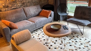 A cozy living room with a stone wall, a sofa, a coffee table, and a view of a forest through a window. - New Le Corbier for 10 p. Renovated top-of-the-range 4bed/2bath/2wc/slope frontage (Villarembert)