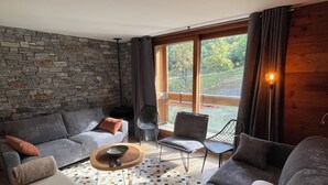 A modern living room with a stone wall, grey sofas, a coffee table, and a view of greenery outside. - New Le Corbier for 10 p. Renovated top-of-the-range 4bed/2bath/2wc/slope frontage (Villarembert)