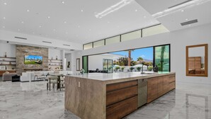 A spacious, modern kitchen with a large island, a dining area, and a living space with a large TV and fireplace.