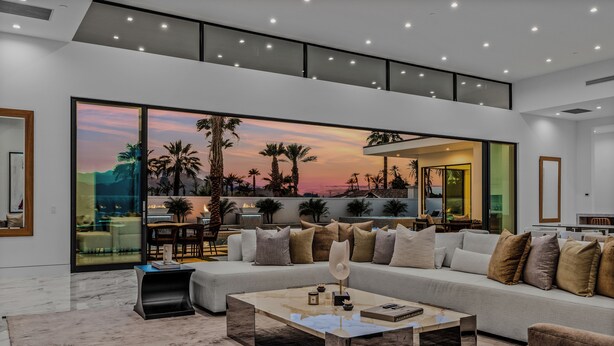 A modern living room with a large window, a sofa, a coffee table, and a view of a sunset.