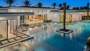 A modern pool area with a clear view of the pool, surrounding lounge area, and a building with large windows.