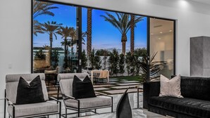 Un salon moderne avec un mur en verre, deux fauteuils gris, un canapé noir et une table basse en marbre.