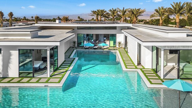 Un espace piscine moderne avec une eau cristalline, entouré de murs de verre et agrémenté d’une terrasse avec des parasols.