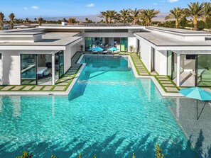 Uma área de piscina moderna, com água cristalina, cercada por paredes de vidro e um terraço com guarda-sóis.
